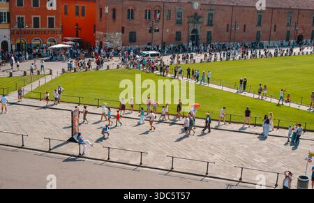 Pisa, Italien - 26. Juni 2025: Touristen spazieren auf den Steinpfaden der Piazza del Duomo in Pisa und bewegen sich auf dem grünen Rasen im Rahmen historischer Gebäude Stockfoto
