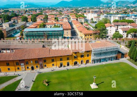 Pisa, Italien - 26. Juni 2025: Blick vom Schiefen Turm auf die Piazza dei Miracoli, mit historischen Gebäuden, einer mittelalterlichen Stadtmauer, grün Stockfoto