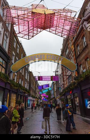 London, Vereinigtes Königreich, 7. Juli 2019: An einem bewölkten Tag besuchen Menschenmassen die Carnaby Street in London. Während weihnachten. Bunte Lichter hängen über der Straße. S Stockfoto