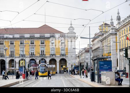 Lissabon Portugal 5. Dezember 2025. Eine moderne gelbe Straßenbahn fährt durch Praca do Comercio, während Fußgänger den Platz überqueren. Stockfoto