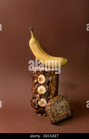Modernes Stillleben mit hausgemachtem Bananenbrot. Brot mit Walnüssen, bestreichen Karamell, belegt mit frischer Banane auf braunem Hintergrund. Levitation Banane abo Stockfoto