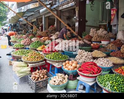 hanoi-Vietnam-10. August 2019, überfüllte Körbe mit Knoblauch, Chilis, Limetten und Wurzeln stapelten sich hoch an einem belebten Straßenmarkt in Vietnam, Reflec Stockfoto