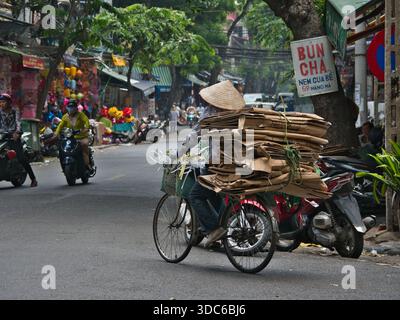 Haoi-10. August 2019, Ein Recycler mit konischem Hut transportiert eine große Ladung gebündelter Pappe auf einem Fahrrad entlang der Hàng MÃ-Straße in der Alten Quarte Stockfoto