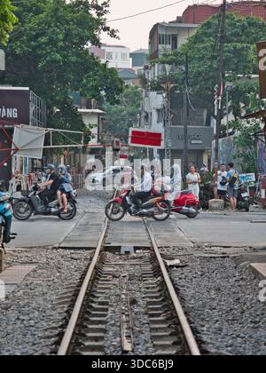 hanoi-Vietnam-10. August 2019: Motorradfahrer fahren an der Bahnüberquerung in einem überfüllten Stadtgebiet von Hanoi, Vietnam. Spiegelt das wahre wider Stockfoto