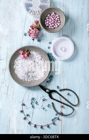 Handgefertigte Schmuckherstellung. Erstellung einer perlenbesetzten Halskette mit Glasperlen und Komponenten in einer Keramikschale. Schere, Schmuckstücke, Frühlingsblumen auf Licht Stockfoto