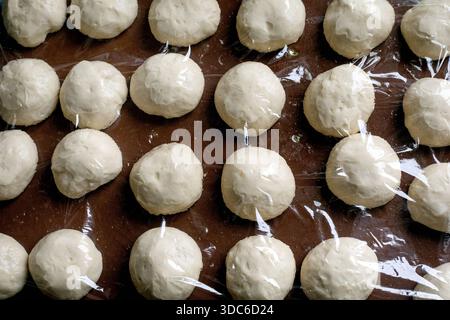 Rohe Teigkugeln mit Kunststofffolie auf brauner Oberfläche. Proofing-Brotteig, der zum Backen von frischem Gebäck zubereitet wird. Stockfoto