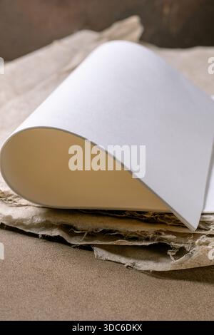 Weißes Papier aus Reis und Maulbeere, das elegant auf braunem, strukturiertem Papierhintergrund gekrümmt ist, zeigt einen Kontrast zwischen glatter weißer Oberfläche und rauem Organi Stockfoto