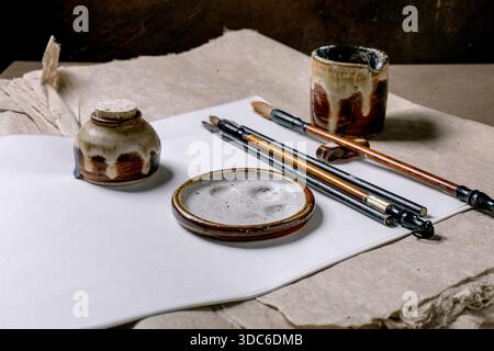Traditionelle chinesische Kalligraphiewerkzeuge auf weißem Reis- und Maulbeerpapier. Steinpinsel mit Keramiktinte und Holzgriffen für orientalische PA Stockfoto
