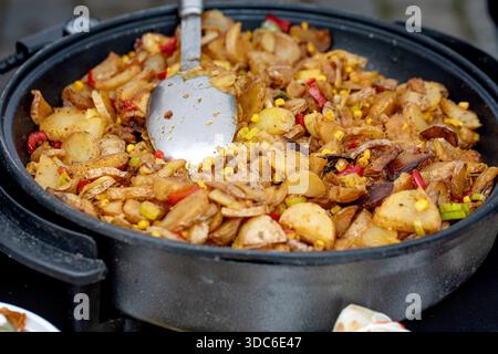 Hausgemachte Pfanne mit Kartoffeln, Paprika und Zwiebeln, die in einer schwarzen gusseisernen Pfanne mit Spachtel gekocht werden. Köstliches Gemüsegericht, das im Freien zubereitet wird Stockfoto