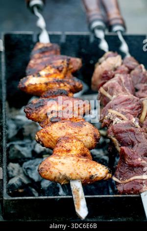 Nahaufnahme von gewürzten Hühnchen- und Rinderspießen, die auf Holzkohlegrill kochen. Rauchiges Fleisch mit Gewürzen, das draußen gegrillt wird. Perfekt für Grillpartys im Sommer. Stockfoto