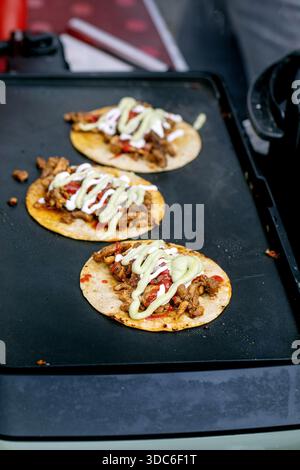 Hausgemachte mexikanische Street Tacos mit Fleisch Tomaten, weißer Creme und Avocadosauce, die auf schwarzem Grill gekocht werden. Traditionelle lateinamerikanische Küche. Stockfoto