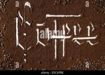 Kalligraphische Inschrift gotische Buchstaben Kaffee über gemahlenem schwarzem Kaffee verstreut auf weißem Marmor mit gerösteten Bohnen. Hintergrund des Kaffeetrinkkonzepts. Draufsicht Stockfoto