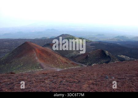 Vulkanischer Krater auf dem Ätna in Sizilien mit dunklen Lavahängen, zerklüftetem Gelände und einer Straße, die im Hintergrund am Rand sichtbar ist Stockfoto