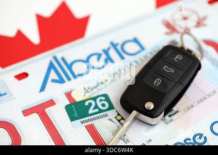 Alberta canadian Autokennzeichen und Zündschlüssel auf der Flagge von Kanada Nahaufnahme. Führerschein- und Zulassungskonzept Stockfoto
