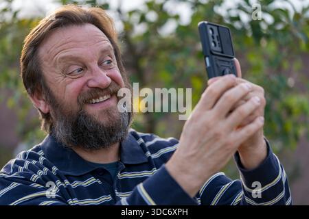 Glücklicher Seniorenmann Ruhe in der Natur Erhalten Sie eine Nachricht von einem alten Freund. Reifer Mann, der gute Nachrichten auf dem Telefon liest. Älterer Mann mit Handy Stockfoto