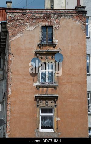 Altes Mietshaus in schlechtem Zustand mit Satellitenschüsseln an der Wand Stockfoto