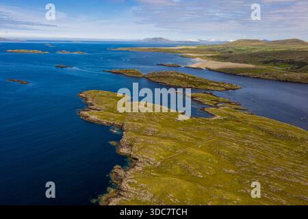 Weitläufiger Blick aus der Luft auf eine zerklüftete Küstenlandschaft mit grünen Klippen, felsigen Felsvorsprüngen und ruhigen blauen Gewässern, Galway, Irland Stockfoto
