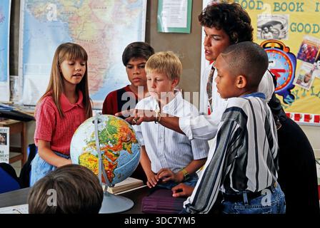Die Schüler treffen sich rund um den Globus, während ein Lehrer auf verschiedene Länder hinweist. Das Ambiente zeigt das aktive Engagement für eine Lernerfahrung in einem Clas Stockfoto