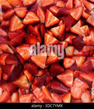 Frische Erdbeeren werden in kleine Scheiben geschnitten und eng aneinander auf einer Ebenen Oberfläche platziert. Die leuchtende rote Farbe zeigt die Frische der Früchte. Stockfoto