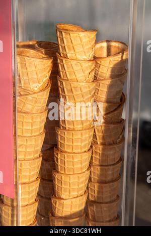 Stapelweise Waffelkegel hinter einer Glasvitrine in einem Straßencafé bei warmem Sonnenlicht. Saubere leere Halter bereit für den Eisservice, die an Sommererfrischungen und süße Nachspeisen erinnern Stockfoto