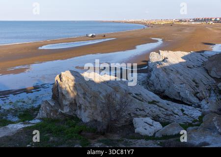 Eine ruhige Küstenlandschaft mit großen Felsen im Schatten, einer sandigen Küste und einem ruhigen Blick auf das Kaspische Meer unter weichem Himmel. Buzowna, Aserbaidschan Stockfoto