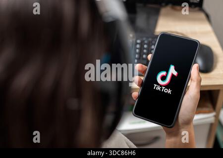 Ein nicht erkennbarer weiblicher Teenager hält ein Handy mit einem Tik Tok-Logo auf dem Bildschirm mit schwarzem Hintergrund Stockfoto