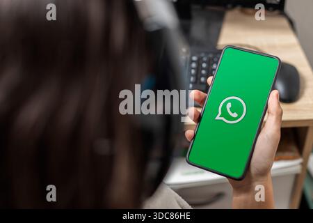 Ein nicht erkennbarer weiblicher Teenager hält ein Mobiltelefon mit dem Whatsapp-Logo auf dem Bildschirm mit grünem Hintergrund Stockfoto