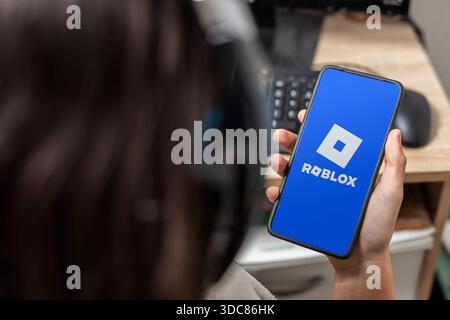 Ein nicht erkennbarer weiblicher Teenager hält ein Handy mit dem Roblox-Logo auf dem Bildschirm mit blauem Hintergrund Stockfoto