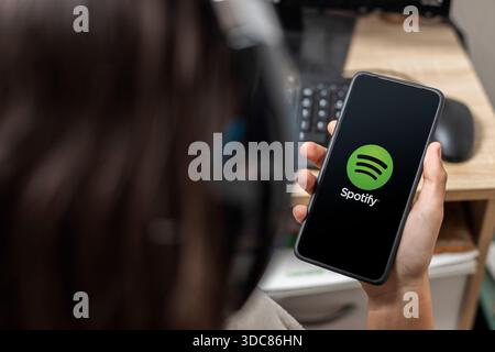 Eine nicht erkennbare Teenagerin hält ein Mobiltelefon mit dem Spotify-Logo auf dem Bildschirm mit schwarzem Hintergrund Stockfoto