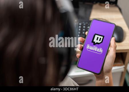 Ein nicht erkennbarer weiblicher Teenager hält ein Mobiltelefon mit einem Zuckungslogo auf dem Bildschirm mit violettem Hintergrund Stockfoto