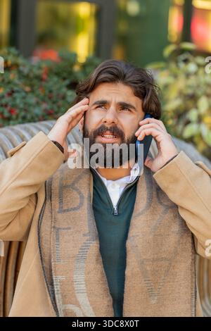 Indischer junger Geschäftsmann Tourist mit schlechten stressigen Nachrichten, die per Smartphone anrufen. Traurig frustriert, verwirrt, hispanisch bärtiger Kerl haben ein Problem unangenehme Ferngespräche auf der Innenstadt Straße Stockfoto
