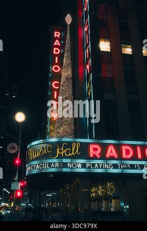 Die Radio City Music Hall leuchtet nachts mit Neonschildern entlang der Sixth Avenue in Midtown Manhattan, New York City. Stockfoto