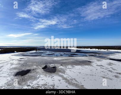 Ein weites, hohes Bild zeigt einen Fluss, der teilweise von Eis und Sumpf bedeckt ist und sich in Richtung eines dunklen, weit entfernten Baumrandes unter einem hellblauen Sch erstreckt Stockfoto