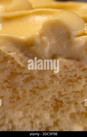 Eine detaillierte Nahaufnahme eines gelben Desserts mit einem glatten, cremigen Topping und einer leichten, luftigen, strukturierten Kuchenschicht darunter. Stockfoto