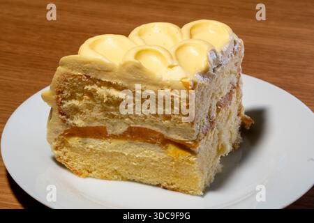 Eine Nahaufnahme einer einzelnen Schicht Kuchen mit einer Füllung aus Schwamm, Sahne und Orangenfrüchten, präsentiert auf einem weißen Gericht. Stockfoto