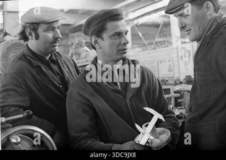 Slaviansk, Ukrainische SSR, UdSSR – 1981: Archivfoto, das einen Facharbeiter in einer Baskenmütze zeigt, die einen Messschieber benutzt, um ein mechanisches Flügelrad zu messen. Zwei Kollegen in flachen Kappen beobachten den Qualitätskontrollprozess in der Werkshalle. Die Szene beleuchtet Feinmechanik und technisches Know-how in der friedlichen Donbass-Region während der späten Sowjetzeit. Stockfoto