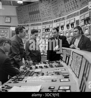 Slaviansk, Ukrainische SSR, UdSSR – 1981: Archivfoto, das den Abgeordneten Rypalenko bei einem Treffen mit Ingenieuren im Hauptkontrollraum eines Kraftwerks zeigt. Gekleidet in einem formellen Anzug mit einem Stellvertreterabzeichen hebt er sich unter den Arbeitern in Uniformen hervor. Der Hintergrund ist gefüllt mit massiven Panels mit analogen Anzeigen und Mimik-Diagrammen. Dieses Bild zeigt das Ausmaß der sowjetischen Industrieverwaltung und die technische Atmosphäre der friedlichen Donbass-Region während der späten sowjetischen Ära. Stockfoto