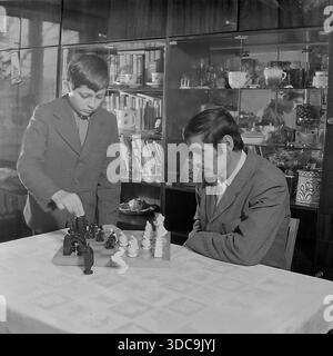 Slaviansk, Ukrainische SSR, UdSSR – 1981: Archiviertes Lifestyle-Foto, das einen Vater und einen Sohn zeigt, der in ein Schachspiel vertieft ist. Der Junge steht über dem Brett, während sein Vater aufmerksam zusieht. Der Hintergrund zeigt eine klassische sowjetische Wandeinheit, gefüllt mit Büchern und Keramik, die die intellektuellen Werte der Familie symbolisieren. Dieses Bild fängt einen Moment der Erziehung und Erziehung in der friedlichen Donbass-Region während der späten Sowjetzeit ein. Stockfoto