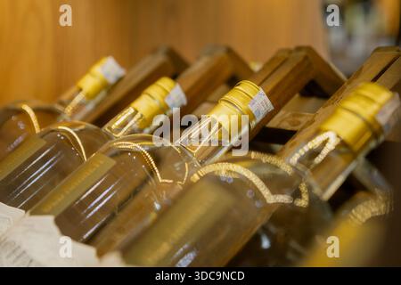 Eine Nahaufnahme, schräge Ansicht mehrerer Glasflaschen mit goldenen Kappen und Halsetiketten, die ordentlich in einem Holzgestell mit geringer Schärfentiefe angeordnet sind Stockfoto