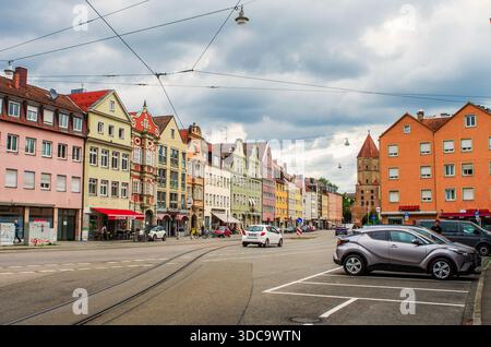 AUGSBURG, DEUTSCHLAND – 14. JUNI 2025: Malerischer Blick auf die Jakoberstraße mit traditionellen bunten Fassaden, geparkten Autos und dem mittelalterlichen Jakobertor-Schlepptau Stockfoto