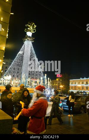 Tbilisi GEO( 20. Dezember 2025 Ein junger Mann, der als Weihnachtsmann verkleidet ist, macht Spielzeug auf dem Freiheitsplatz (vielleicht ist er ein echter Weihnachtsmann?) Stockfoto