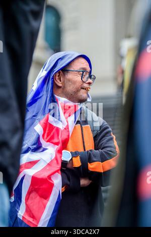 Ein Demonstrant mit einer australischen Flagge über dem Kopf wacht, während er während einer regendurchtränkten Anti-Regierungs-Kundgebung auf den Stufen des Parlamentsgebäudes steht. Rund hundert Demonstranten versammelten sich bei starkem Regen auf den Stufen des Parlamentsgebäudes in Melbourne während einer friedlichen Kundgebung, die zur „Entlassung der Regierung“ nach dem Angriff auf Bondi aufrief. Die Demonstration umfasste Anti-Einwanderungs-Aktivisten, One Nation-Unterstützer und Organisatoren, die zuvor während Melbournes Anti-Lockdown-Proteste bekannt wurden. Die Teilnehmer zeigten australische und israelische Flaggen und beschuldigte Staaten und Bundesstaaten Stockfoto