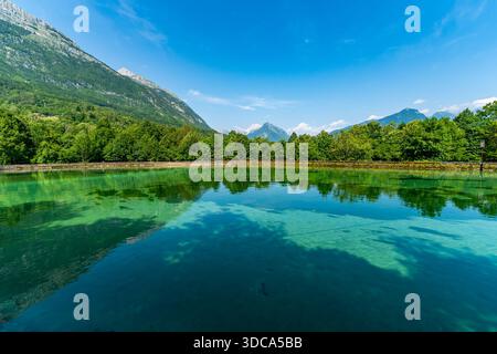 Ruhiges türkisfarbenes Wasser spiegelt üppige Wälder und majestätische Berge unter klarem Himmel wider, was Ruhe und natürliche Schönheit weckt Stockfoto