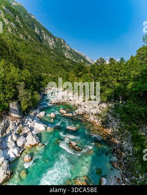 Kristallklares Wasser kaskadiert über glatte Felsen im slowenischen Soca-Tal, was bei hellem Sonnenlicht Ruhe und natürliche Schönheit hervorruft Stockfoto