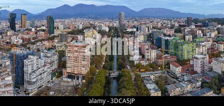 Aus der Vogelperspektive auf Tirana in der Abenddämmerung mit dem Lana River, Wohnvierteln und entfernten Bergsilhouetten. Stockfoto