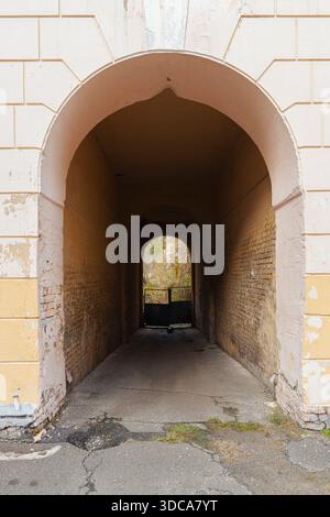Blick durch einen dunklen alten Backsteinbogen in einem alten Stadtgebäude, der zu einem Hinterhof führt. Traditioneller architektonischer Eingang in einem historischen Stadtgebiet Stockfoto