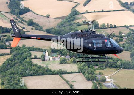 Eine Luft-Luft-Ansicht fängt einen Bell 206B JetRanger III Hubschrauber mit der Registrierung D-HHFW ein, der von Heliteam betrieben wird, während seiner Teilnahme an der Royal International Air Tattoo in Fairford, England. Das Flugzeug erscheint in seiner betrieblichen Lackierung mit seinem zweiflügeligen Haupt- und Heckrotor in Bewegung, wodurch stabile Leistung und Standardkonfiguration erhalten bleiben. Stockfoto
