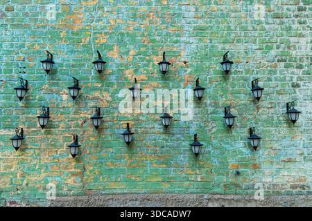 Dekorative Komposition aus mehreren Straßenlaternen aus schwarzem Metall im antiken Stil, die auf einer verwitterten grünen und gelben Ziegelwand montiert sind Stockfoto