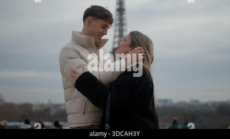 Ein junges Paar umarmt sich liebevoll in Paris Frankreich mit dem Eiffelturm im Hintergrund. Dieses Bild eignet sich für Reisetourismus und Romantik Stockfoto