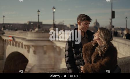 Ein romantisches Paar umarmt sich auf einer Brücke über die seine in Paris Frankreich. Sie tragen Wintermäntel und Jacken und genießen die Aussicht auf die Stadt Stockfoto